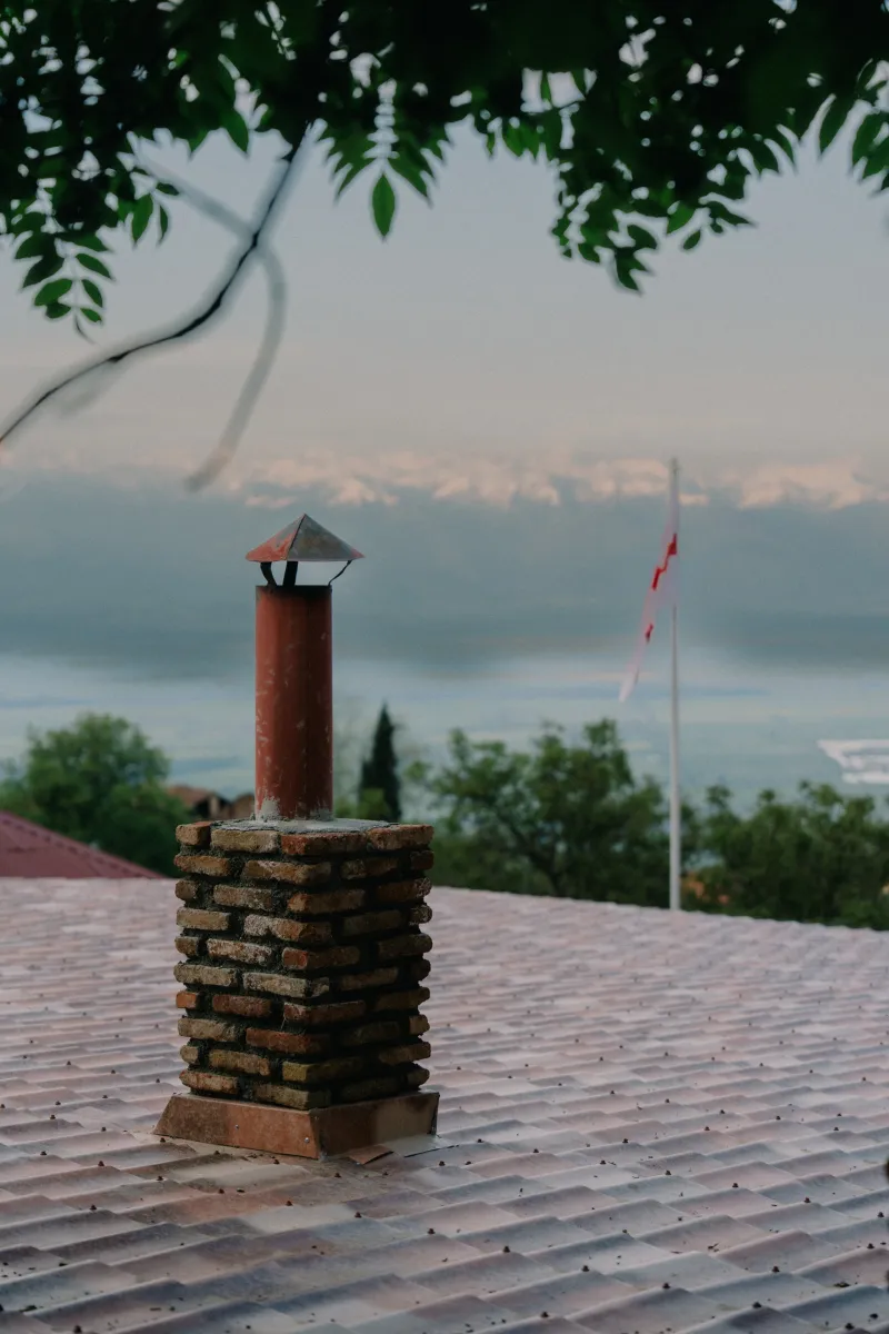 Brick chimney on a tiled roof, Georgian flag and mountains beyond