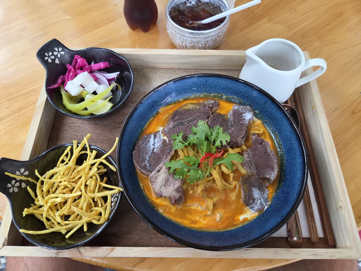 Khao Soi with beef in a blue bowl, crispy noodles and pickles on the side