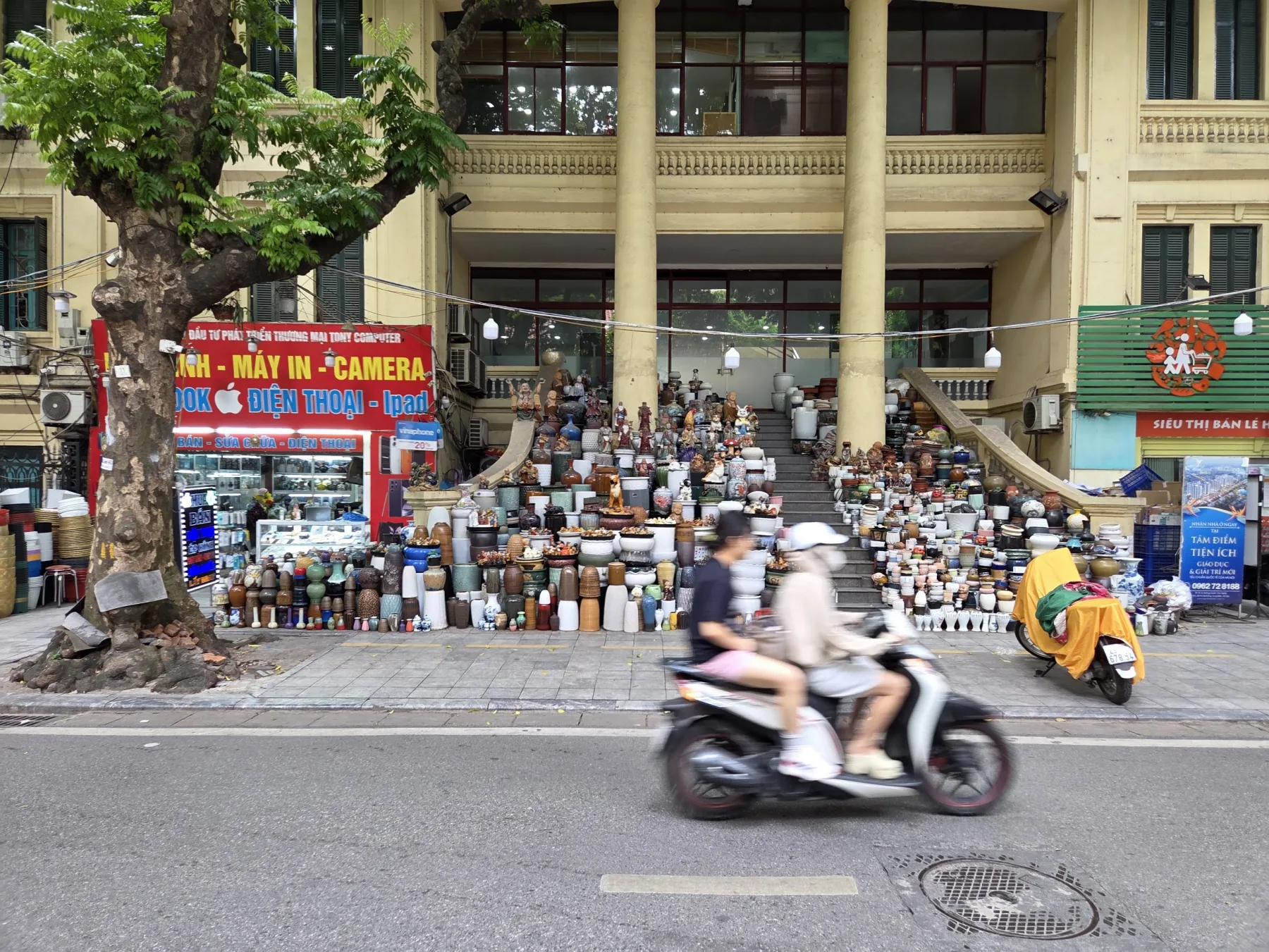 Ceramic pots covering the steps of a Hanoi storefront as a scooter passes