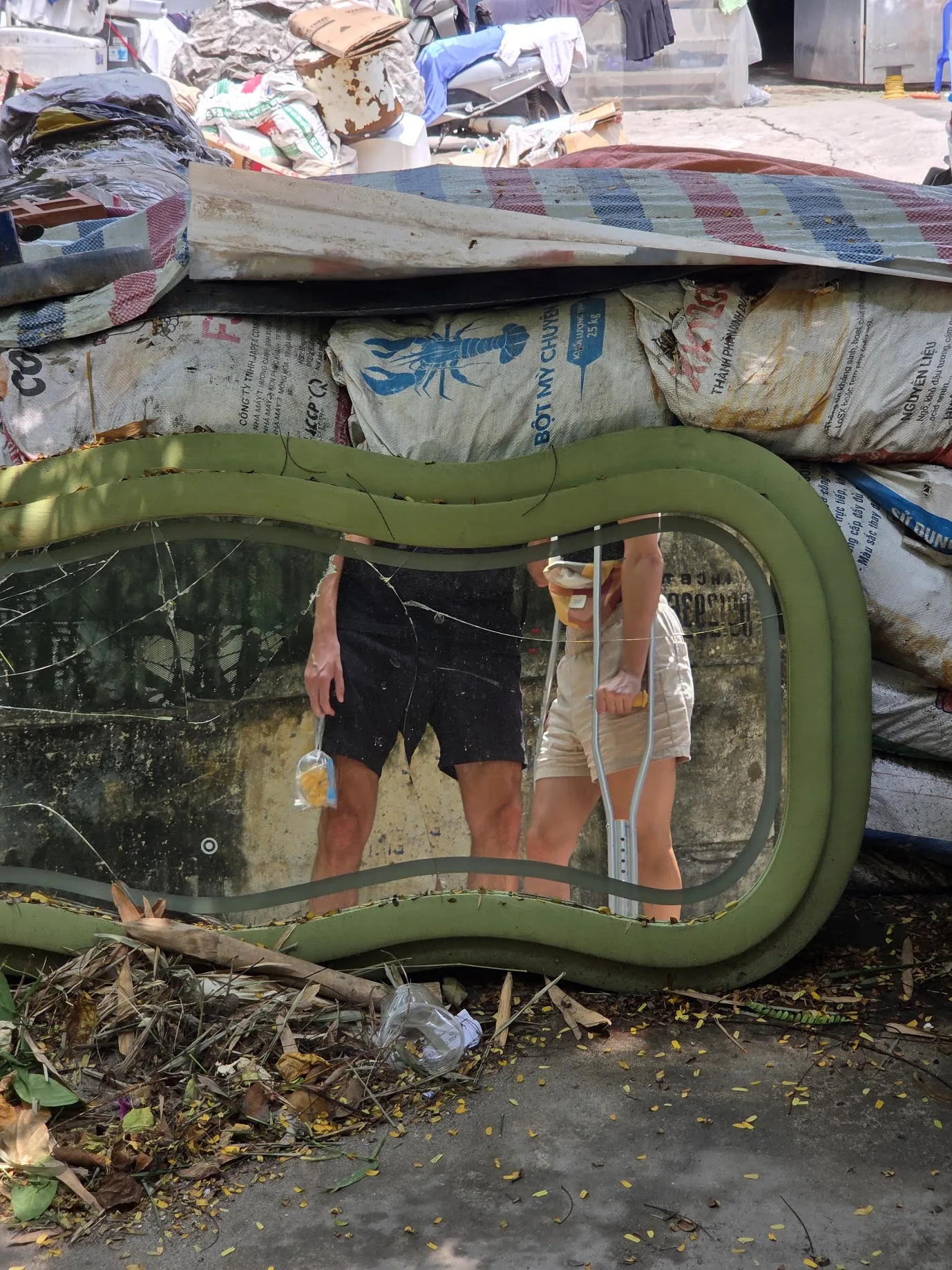 Daniel and Noela reflected in a discarded mirror while Noela is on crutches